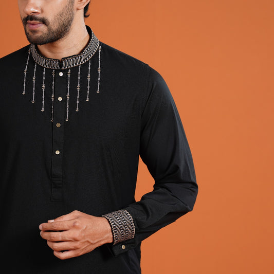 Man wearing a black YAMAAN
traditional outfit with decorative elements on an orange background
