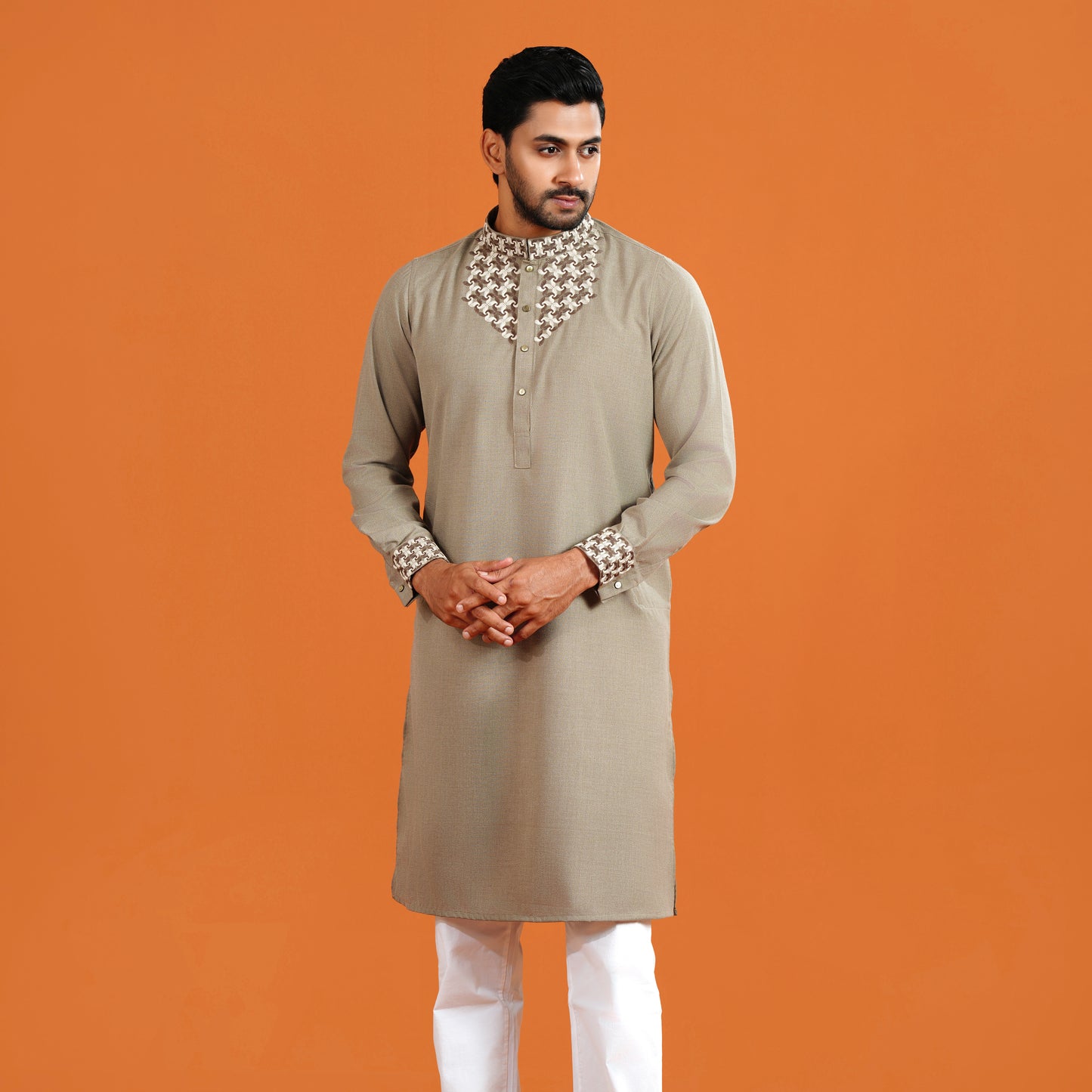 Man wearing a beige kurta with white pants on an orange background