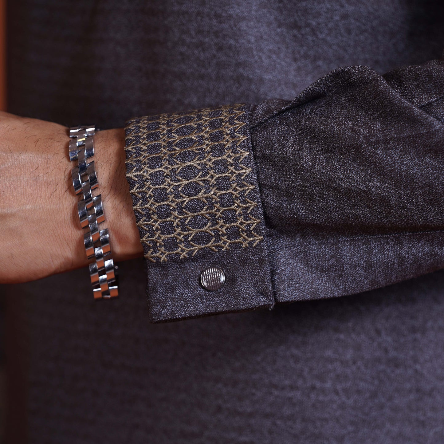 YAMAAN Close-up of a person wearing a dark olive panjabi with patterned cuff and a silver bracelet.