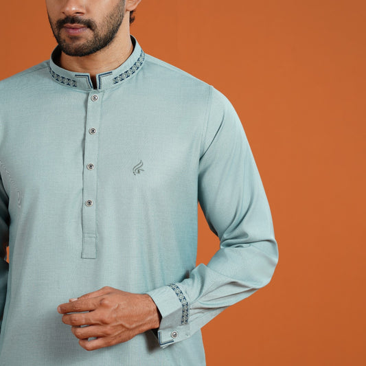 Man wearing a light blue kurta with intricate details on an orange background