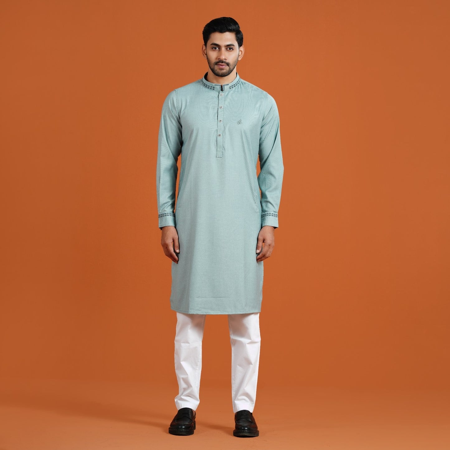 Man wearing a light blue kurta with white pants on an orange background