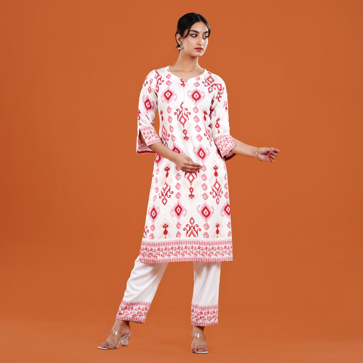 Woman wearing a white and red embroidered kurta with white pants on an orange background