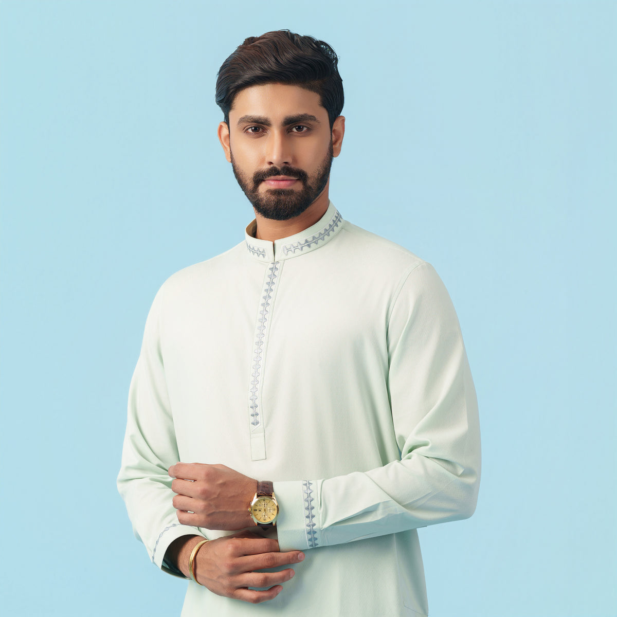 Man wearing a light-colored yamaan panjabi a traditional outfit against a blue background