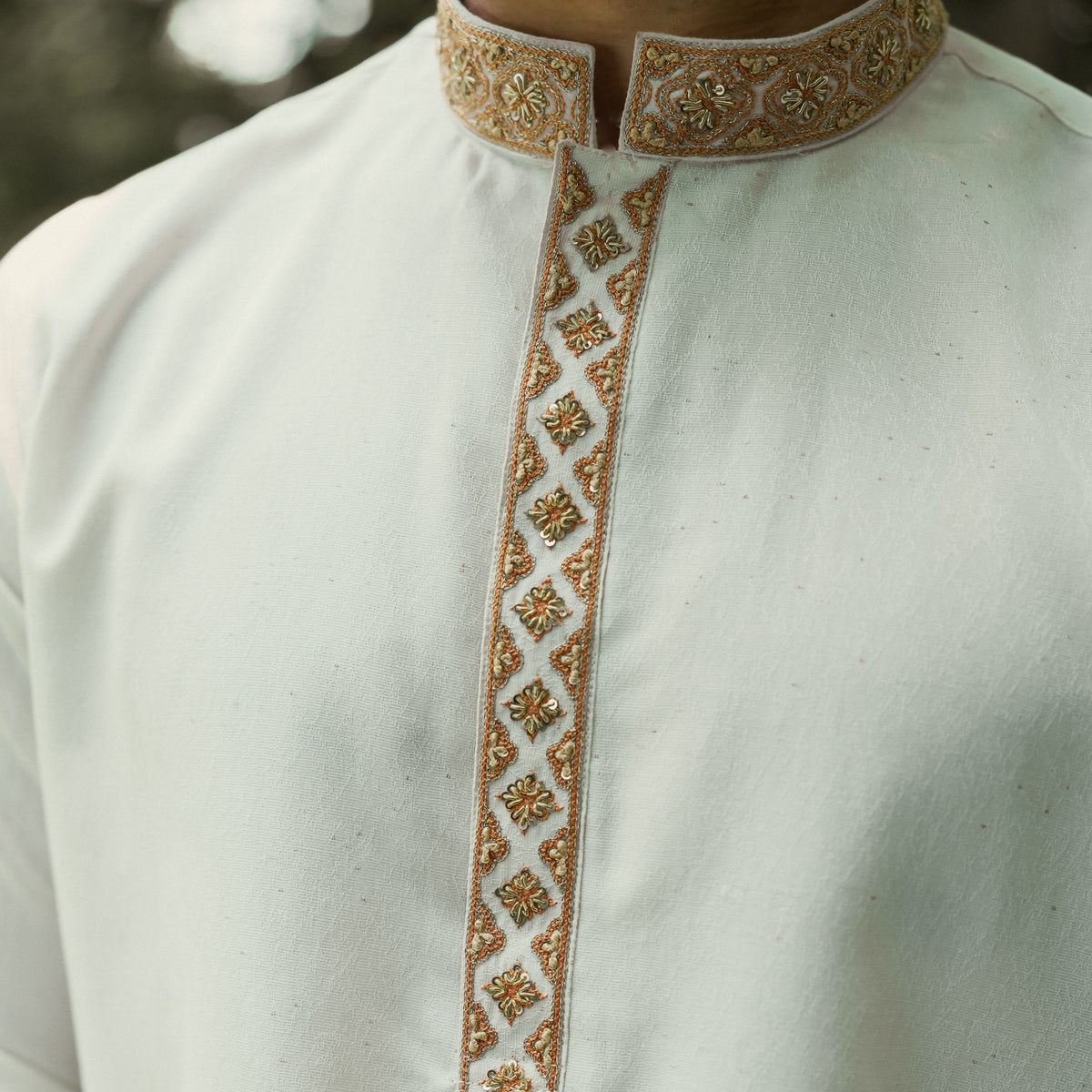 Close-up of a white traditional long-sleeve shirt with ornate gold and brown embroidered trim on the collar and front placket.