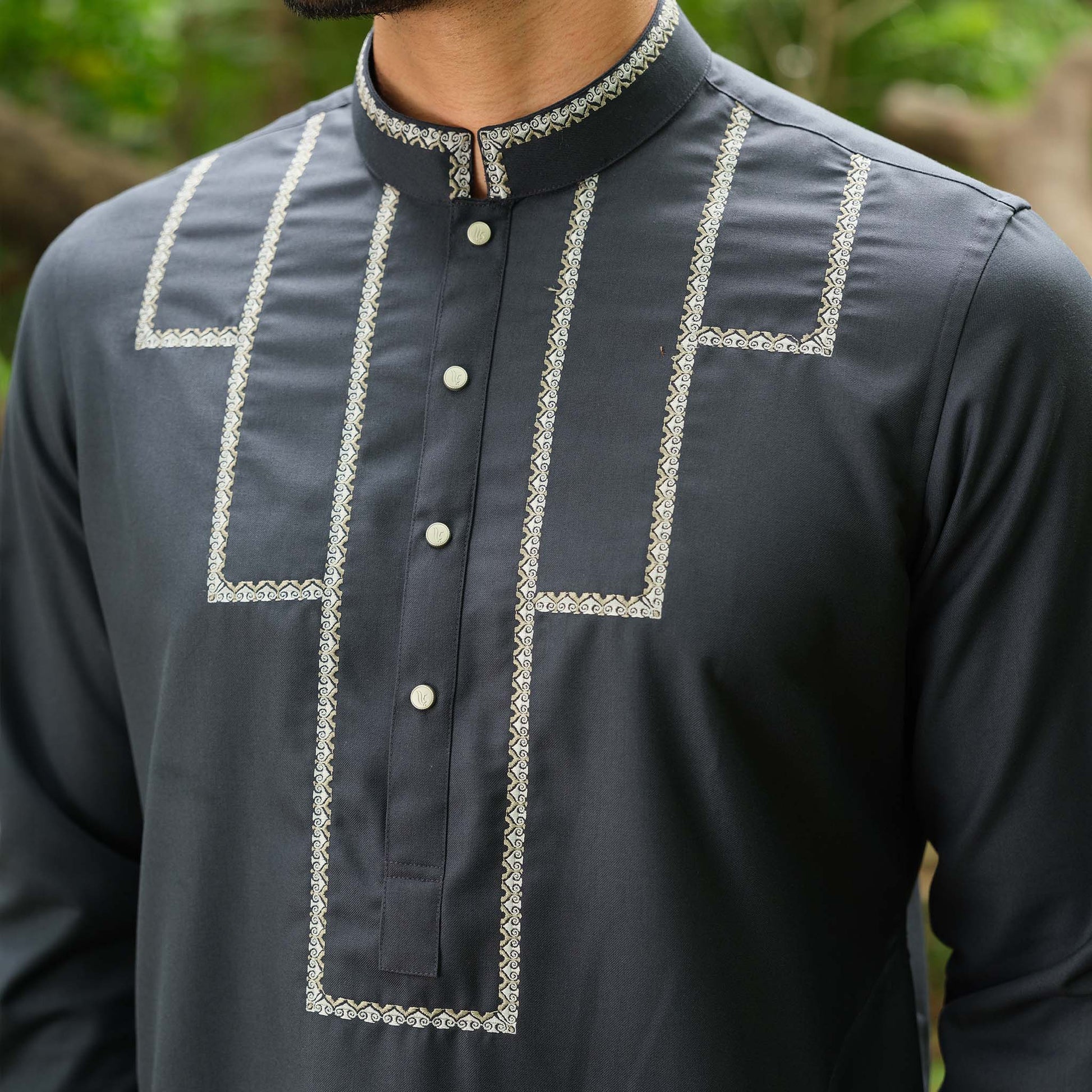 Dark gray shirt with white embroidery details worn by a person, blurred green background