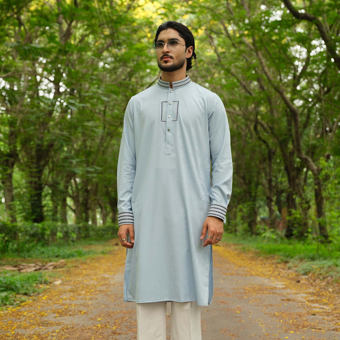 Man wearing a light gray kurta with white pants standing in a forest.