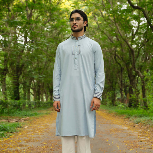 Man wearing a light gray kurta with white pants standing in a forest.