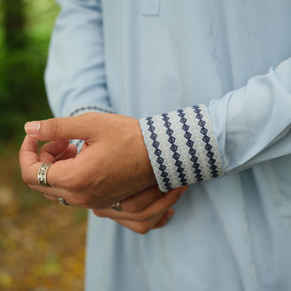 Close-up of a person wearing a patterned sleeve and rings on a blurred natural background