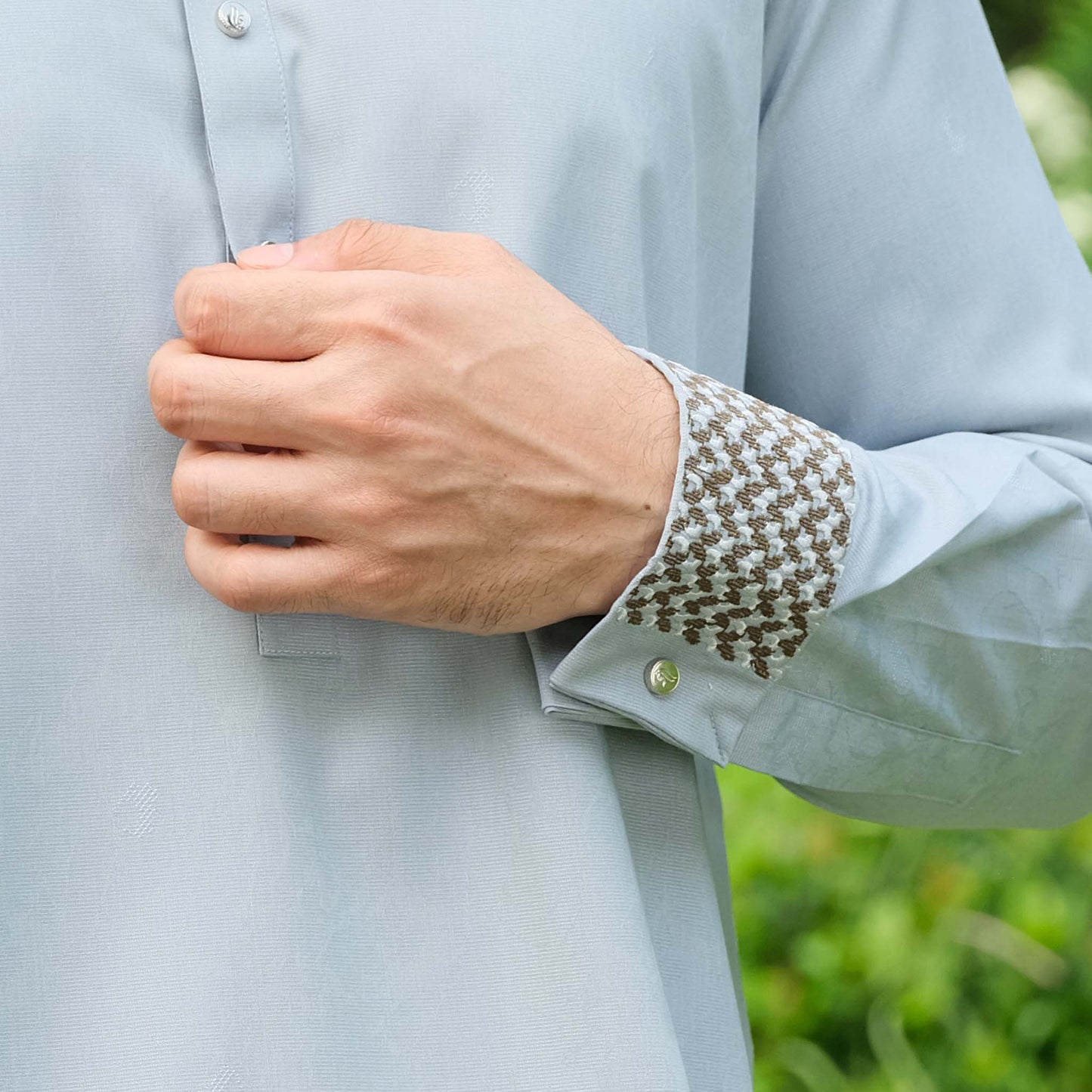 Light blue shirt with patterned cuff and hand adjusting it against a blurred green background