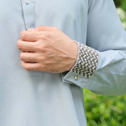 Light blue shirt with patterned cuff and hand adjusting it against a blurred green background