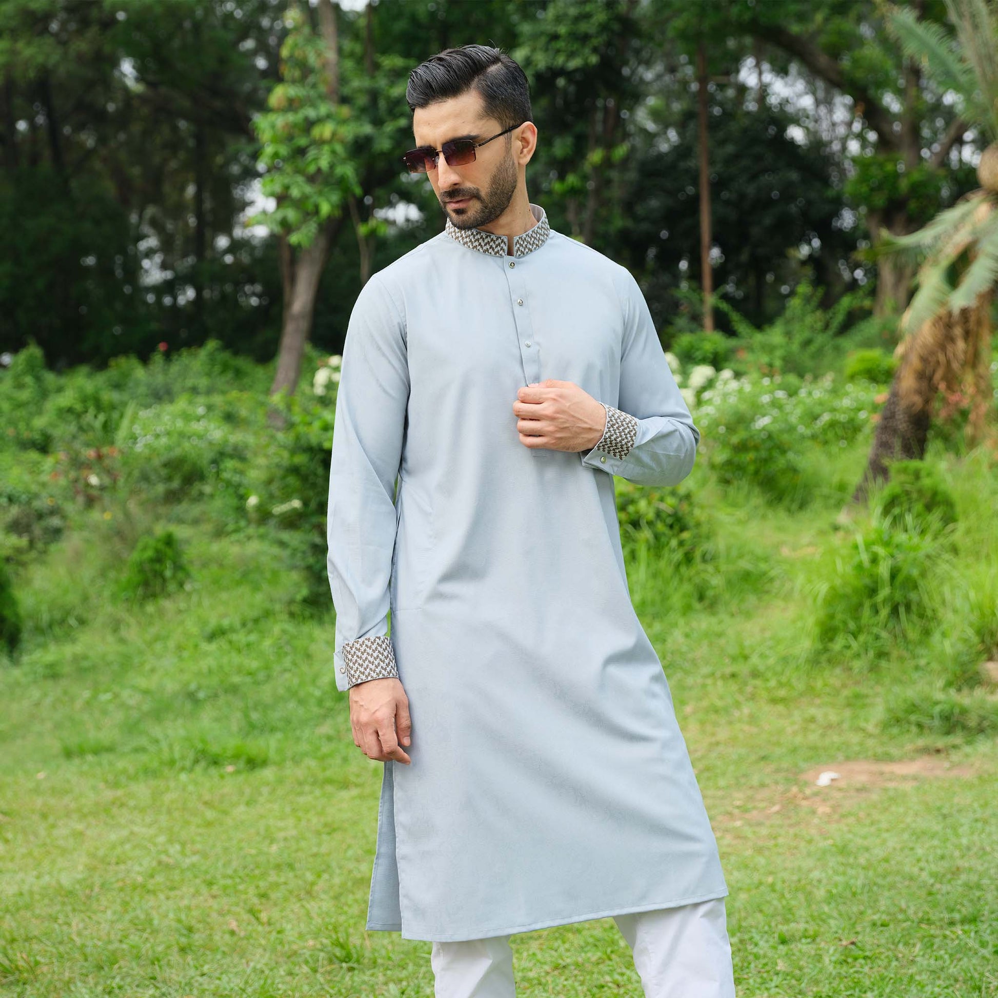 Man wearing a light blue kurta with white pants in a green outdoor setting
