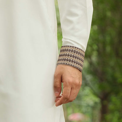Close-up of a person wearing a white garment with a patterned sleeve cuff against a blurred green background.