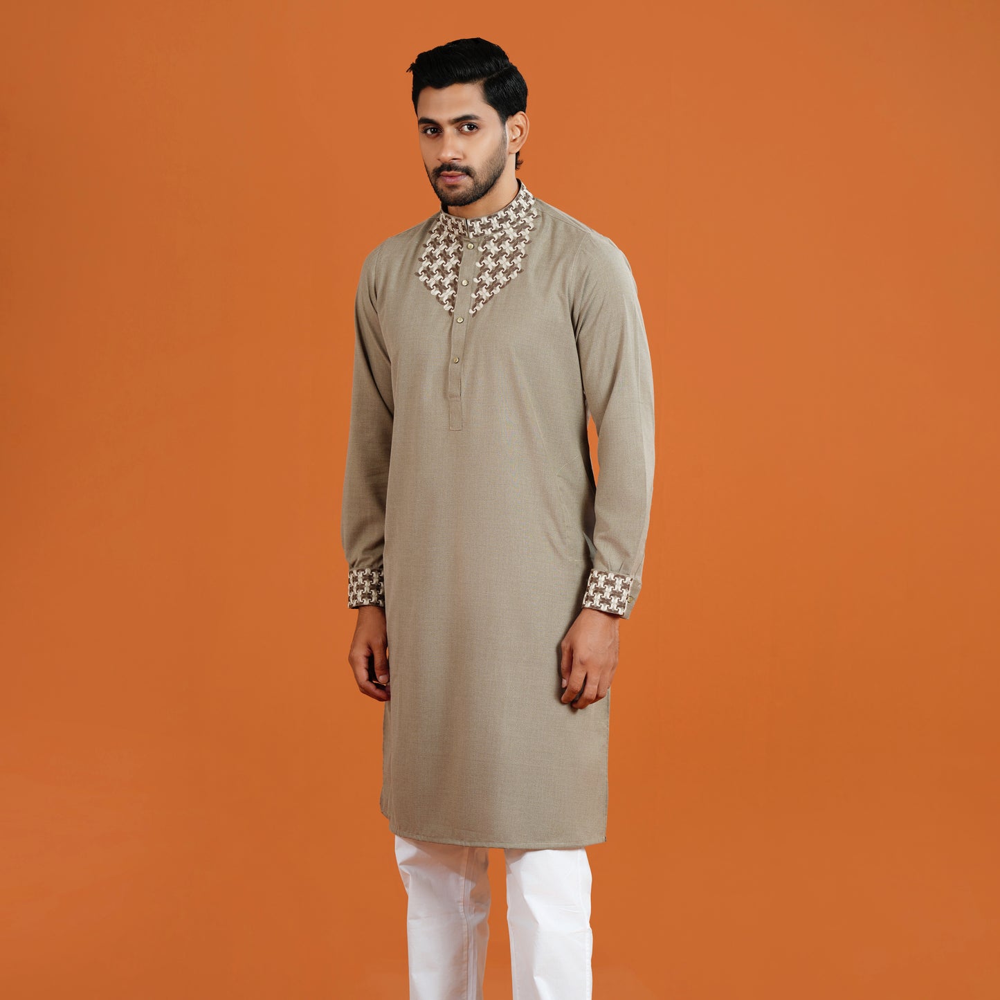 Man wearing a beige kurta with white pants on an orange background