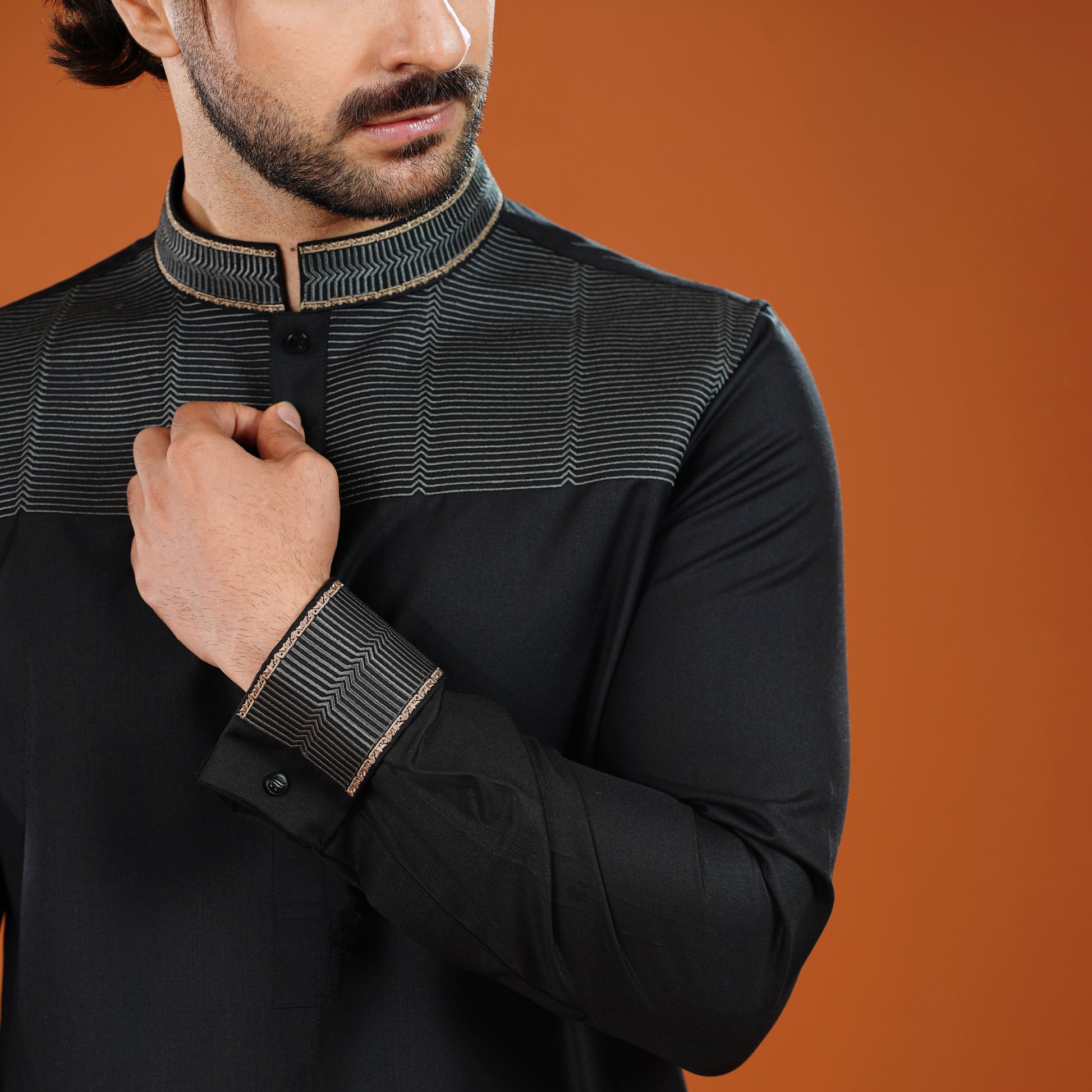 Man wearing a black long-sleeve shirt with intricate detailing on an orange background