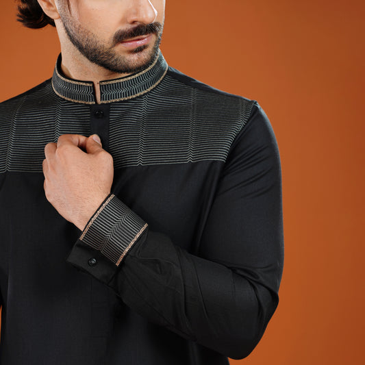 Man wearing a black long-sleeve shirt with intricate detailing on an orange background
