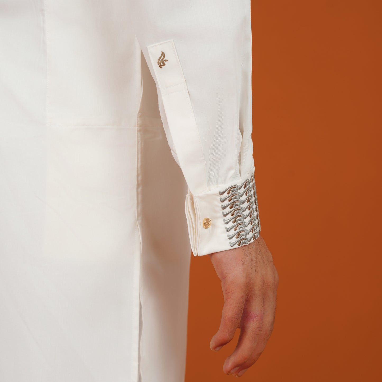 YAMAAN Close-up of a white panjabi with decorative cuffs against an orange background