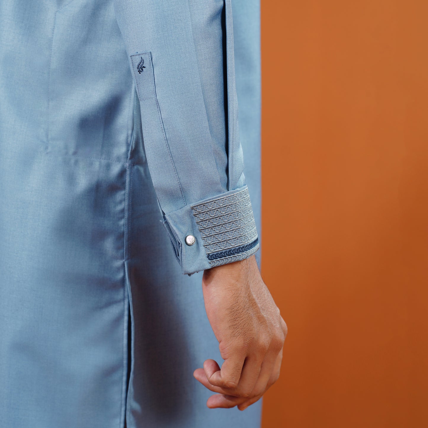 YAMAAN Close-up of a person wearing a light blue panajbi with rolled-up sleeves against an orange background