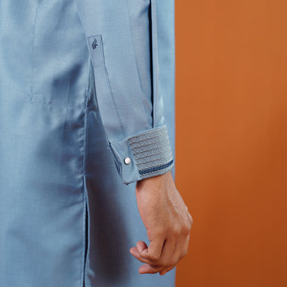 YAMAAN Close-up of a person wearing a light blue panajbi with rolled-up sleeves against an orange background