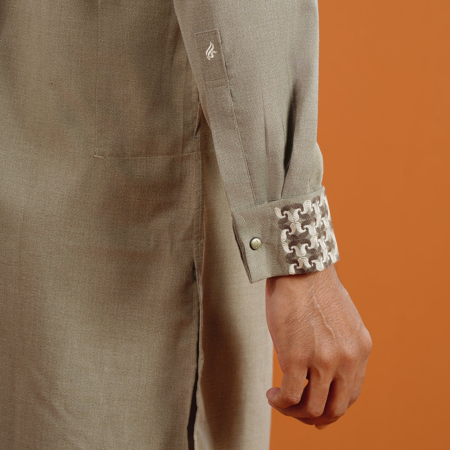 YAMAAN Close-up of a person wearing a green panjabi with a patterned cuff against an orange background