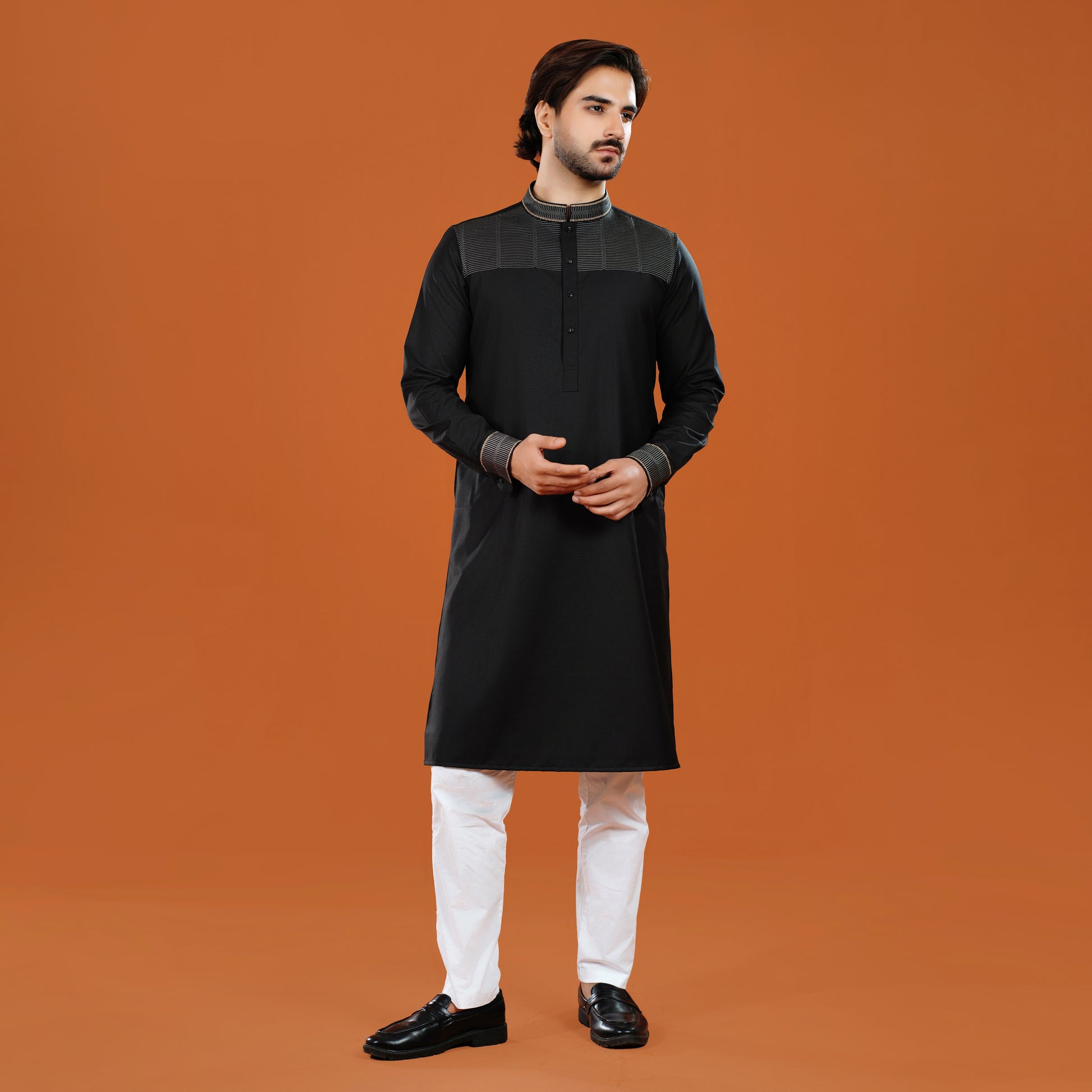 Man wearing a black kurta with white pants on an orange background