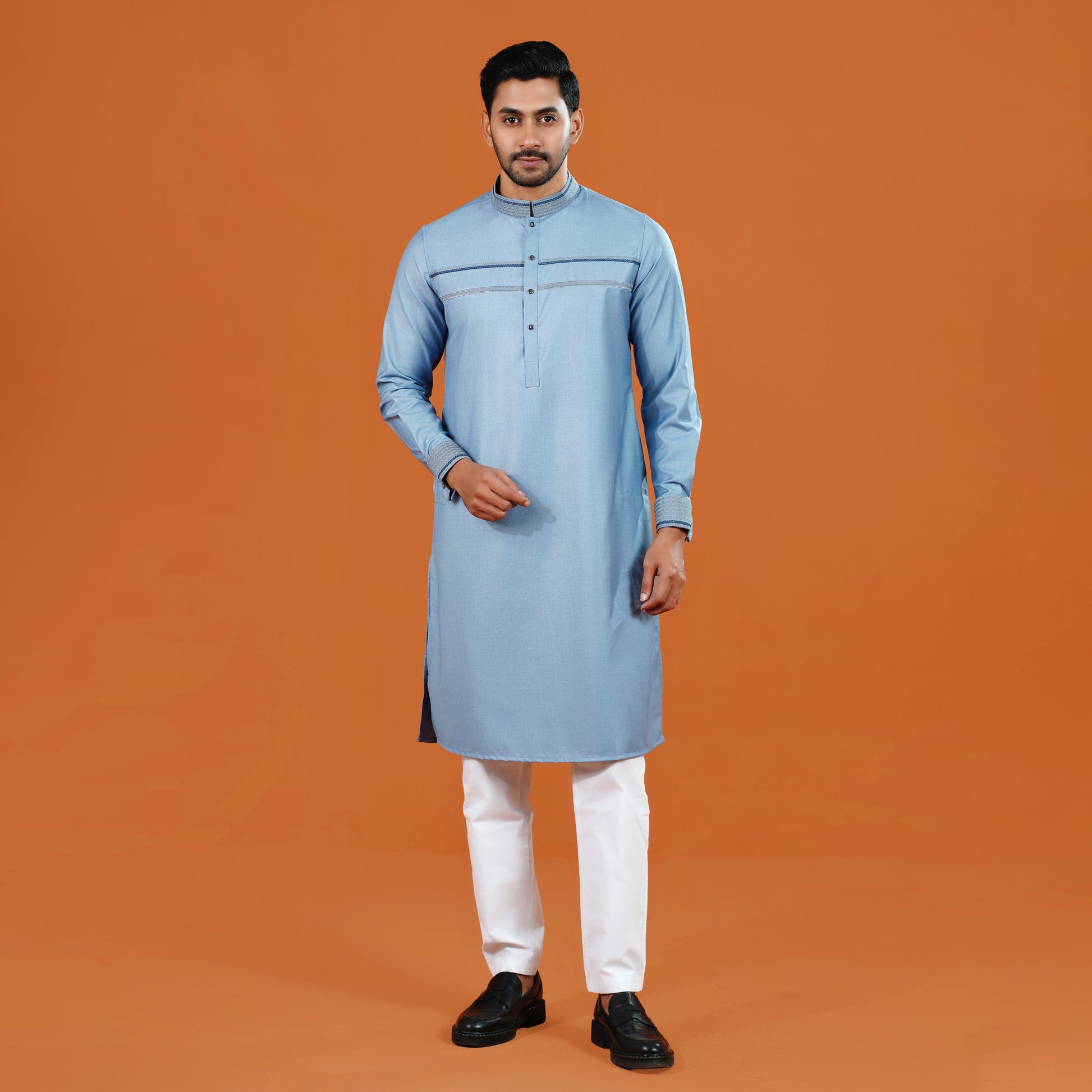 Man wearing a light blue kurta with white pants on an orange background