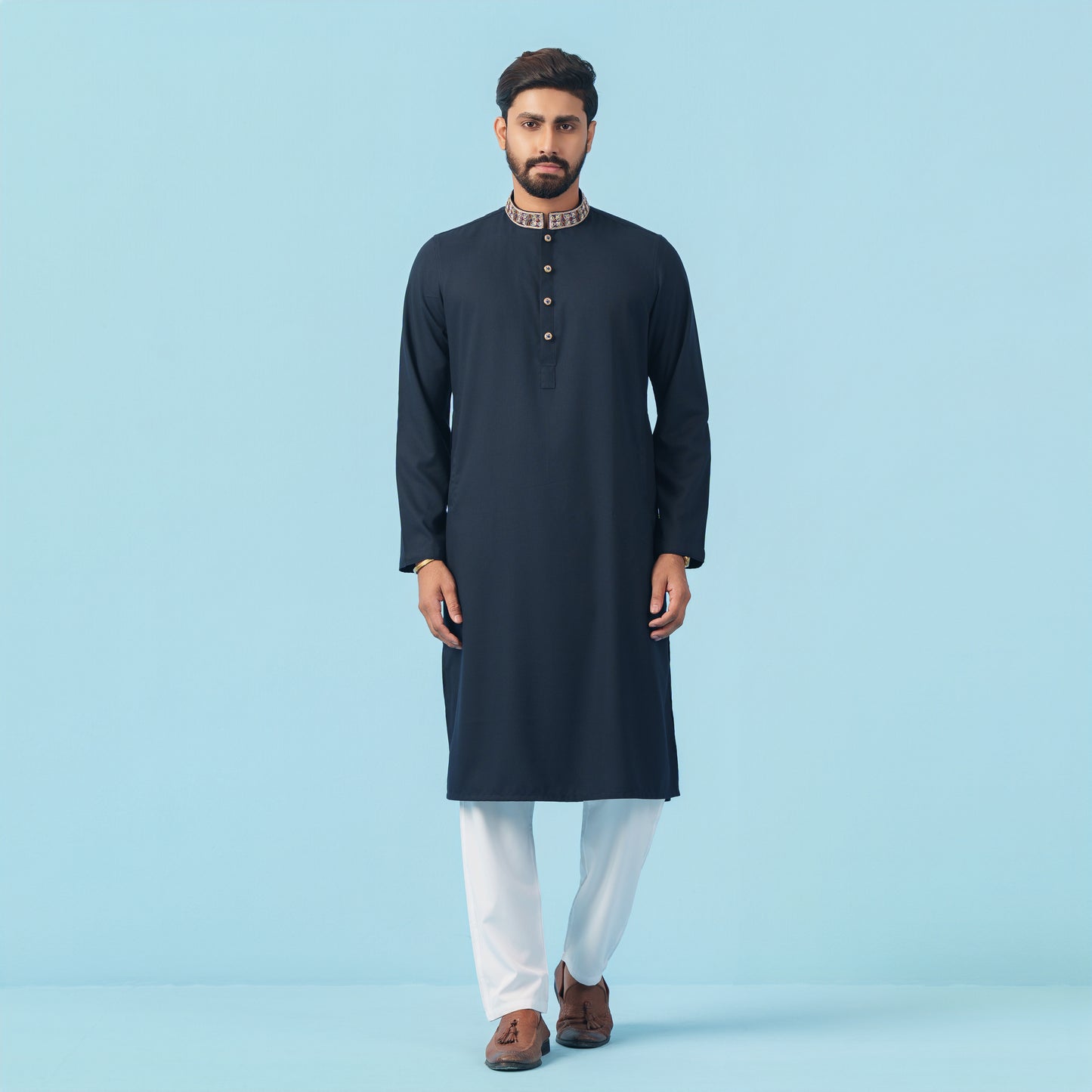 Man wearing a dark blue kurta with white pants on a light blue background