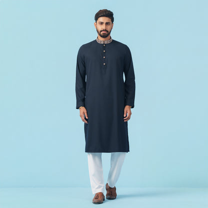 Man wearing a dark blue kurta with white pants on a light blue background
