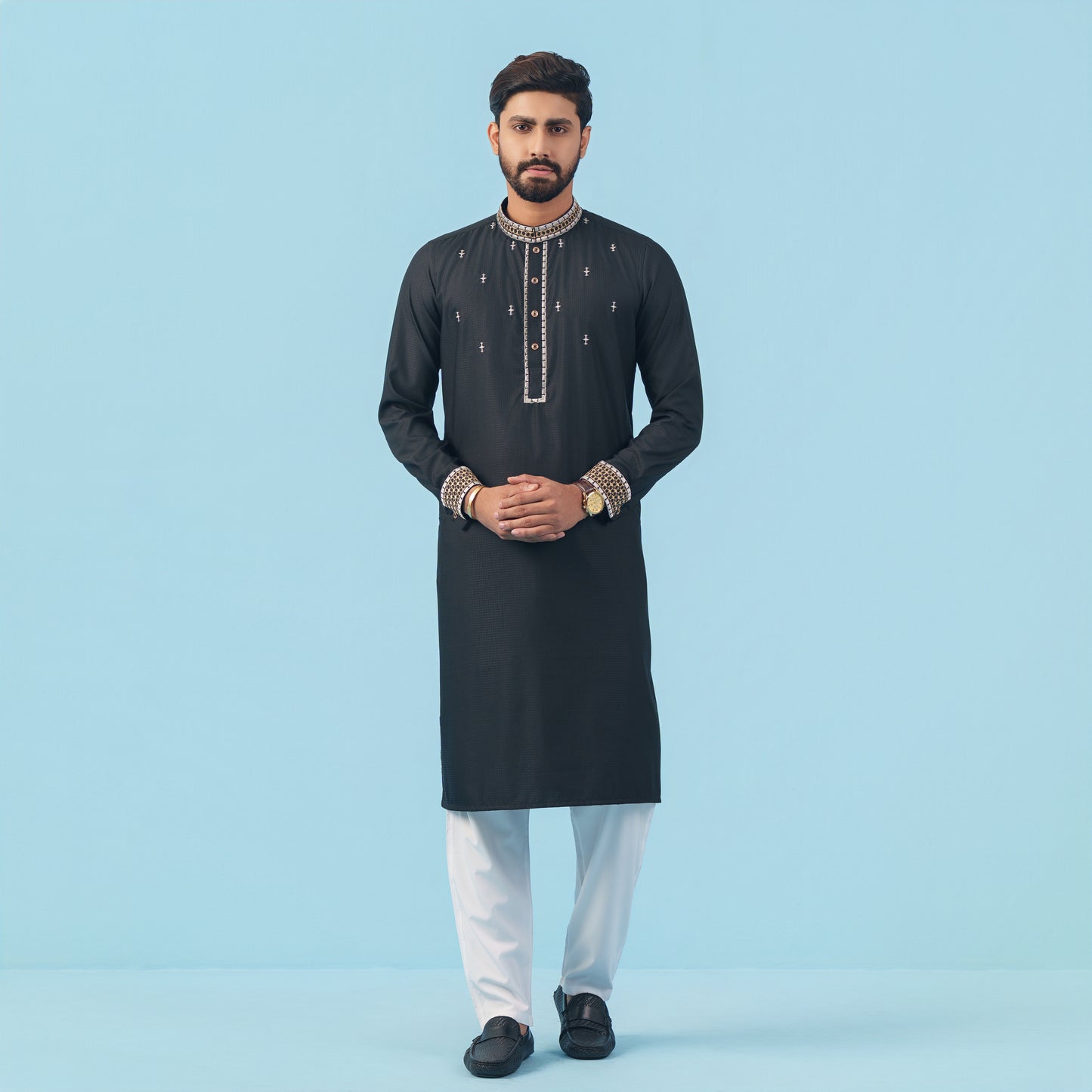 Man wearing a black embroidered YAMAAN kurta with white pants on a light blue background