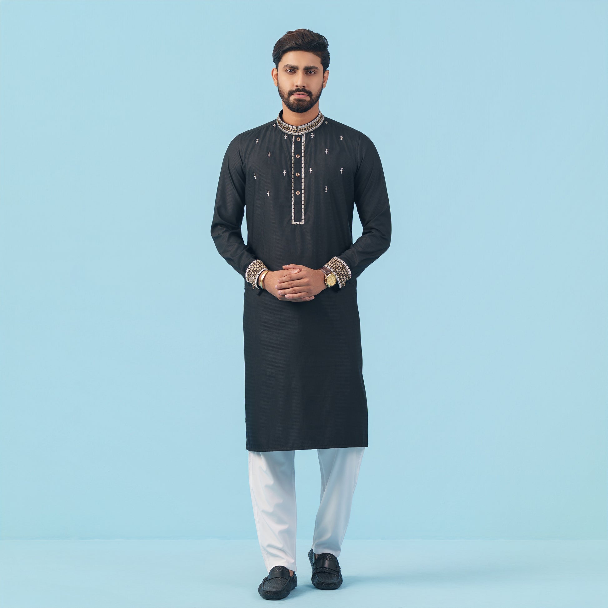 Man wearing a black embroidered YAMAAN kurta with white pants on a light blue background