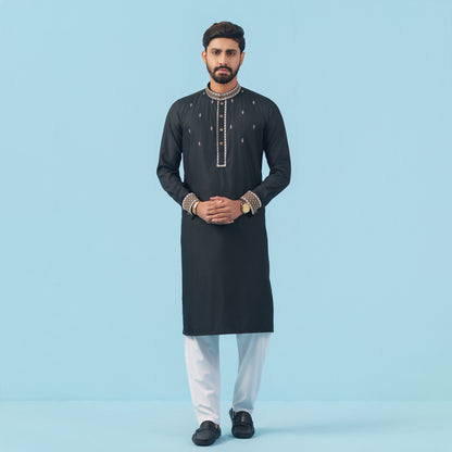 Man wearing a black embroidered YAMAAN kurta with white pants on a light blue background