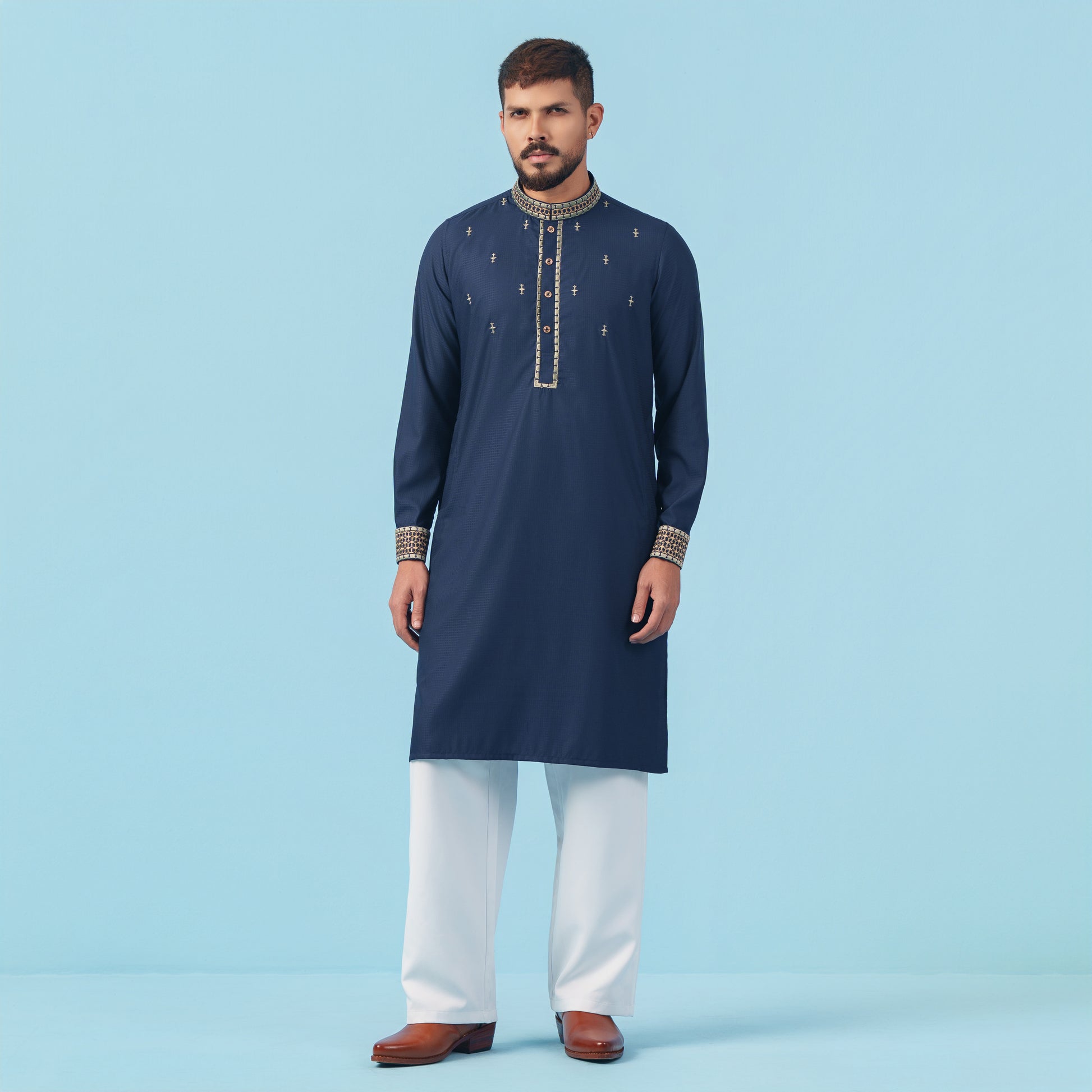 Man wearing a navy blue embroidered YAMAAN kurta with white pants on a light blue background