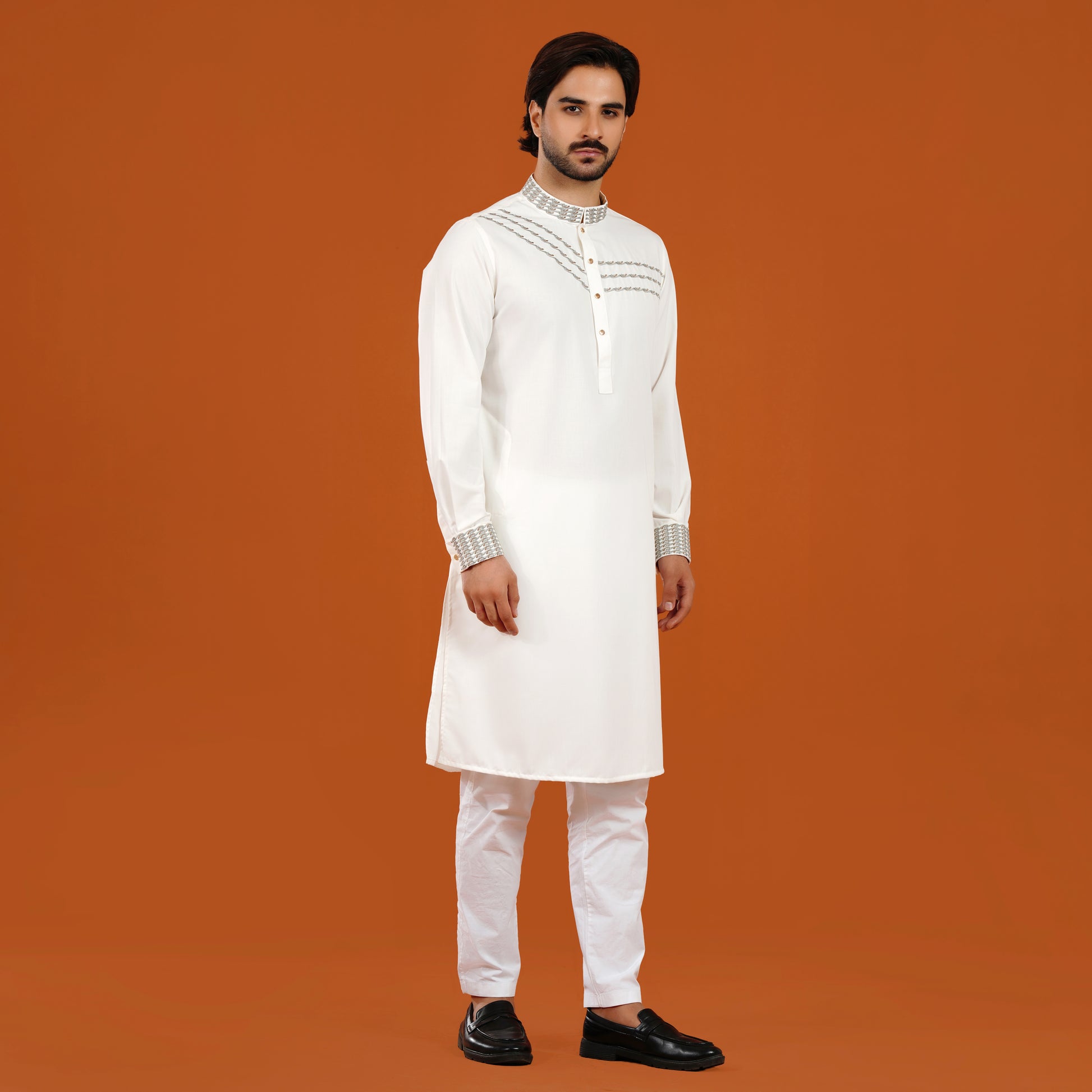 Man wearing a white kurta with embroidery on an orange background