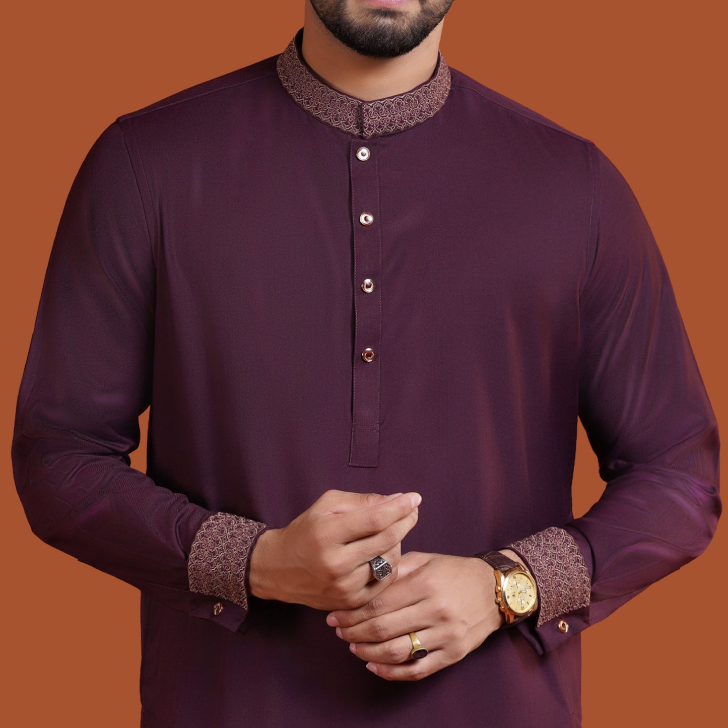 Man wearing a dark maroon YAMAAN traditional outfit with intricate patterns on a brown background