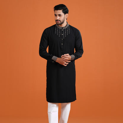 Man wearing a black kurta with white pants against an orange background