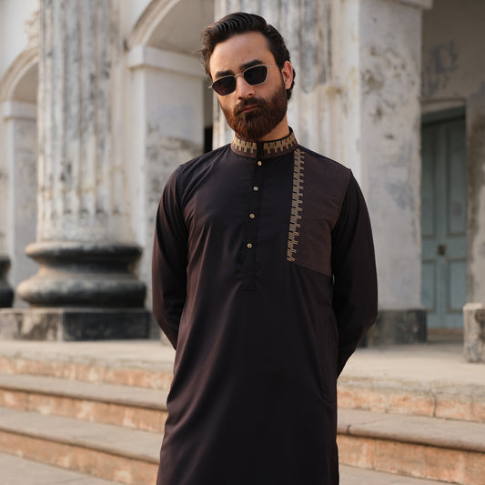 Man wearing a dark traditional outfit with sunglasses in front of classical architecture
