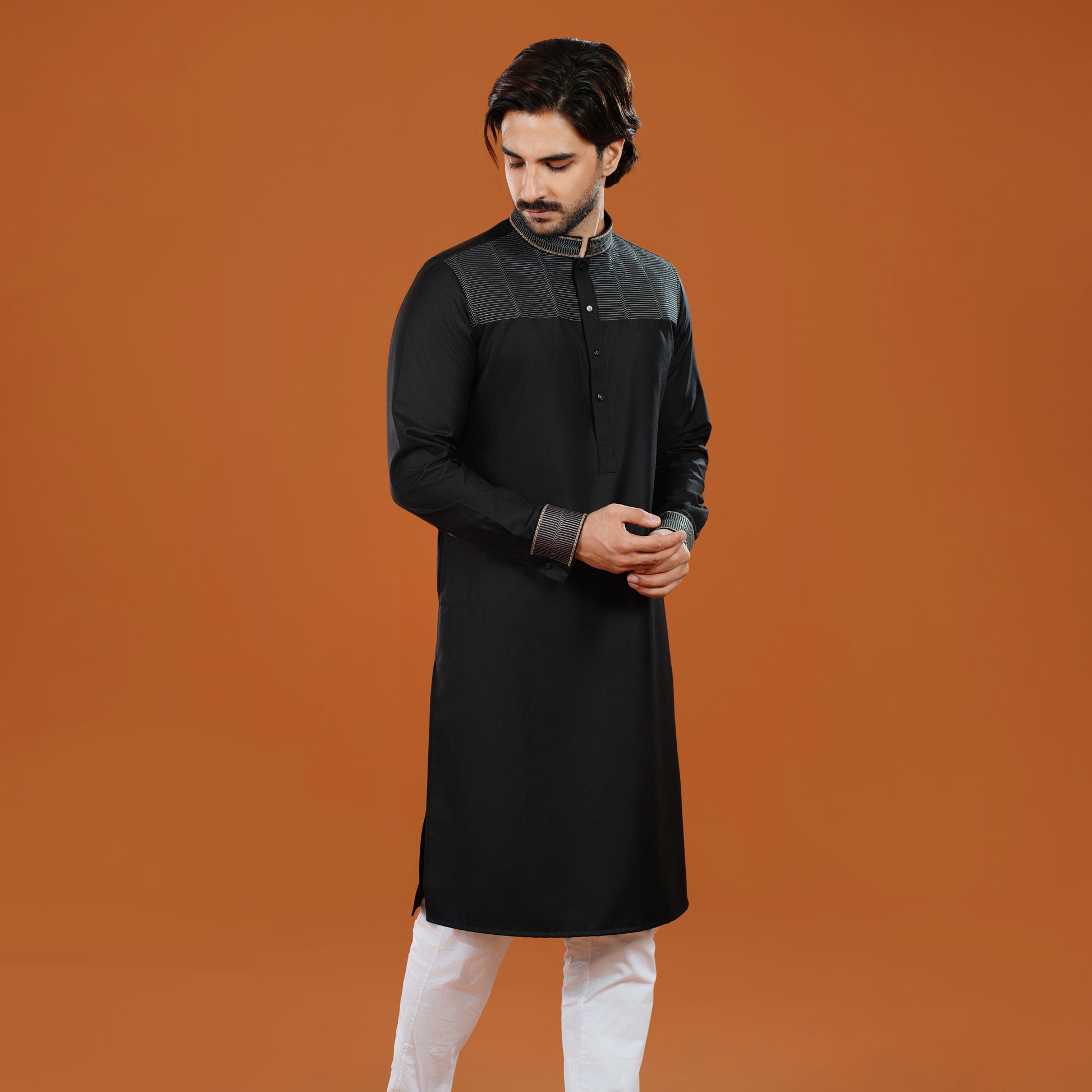 Man wearing a black kurta with white pants on an orange background