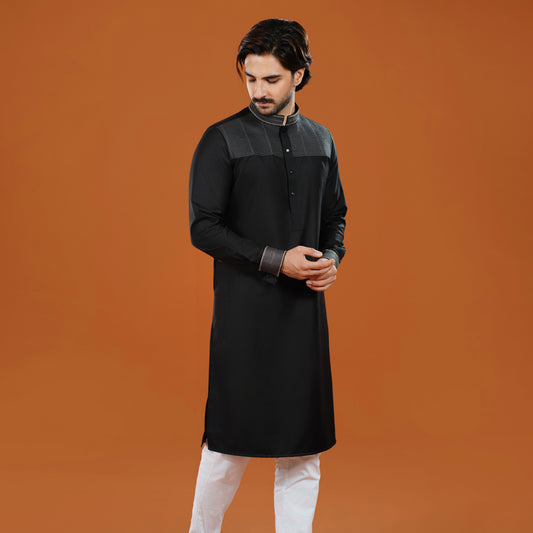 Man wearing a black kurta with white pants on an orange background