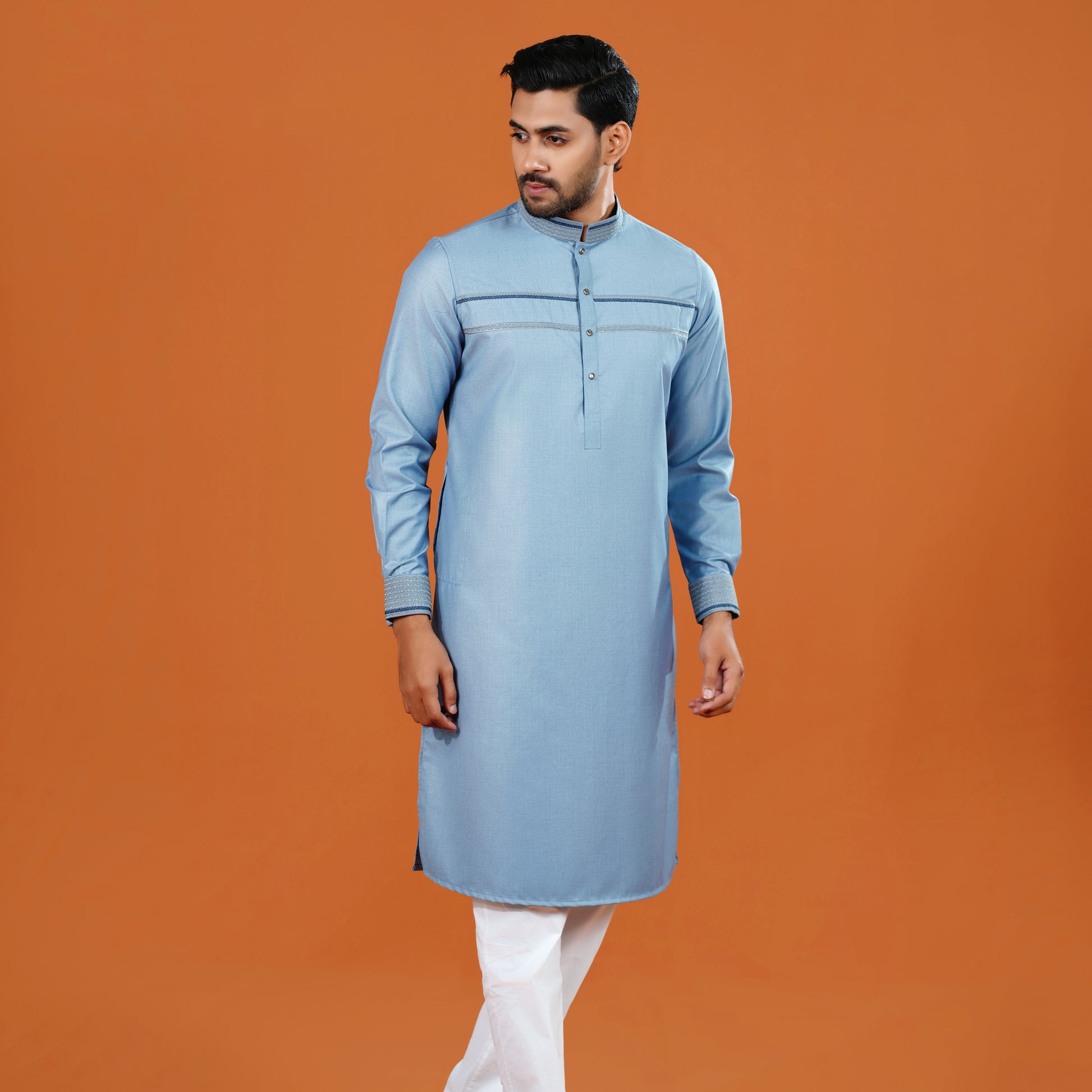 Man wearing a light blue kurta with white pants on an orange background