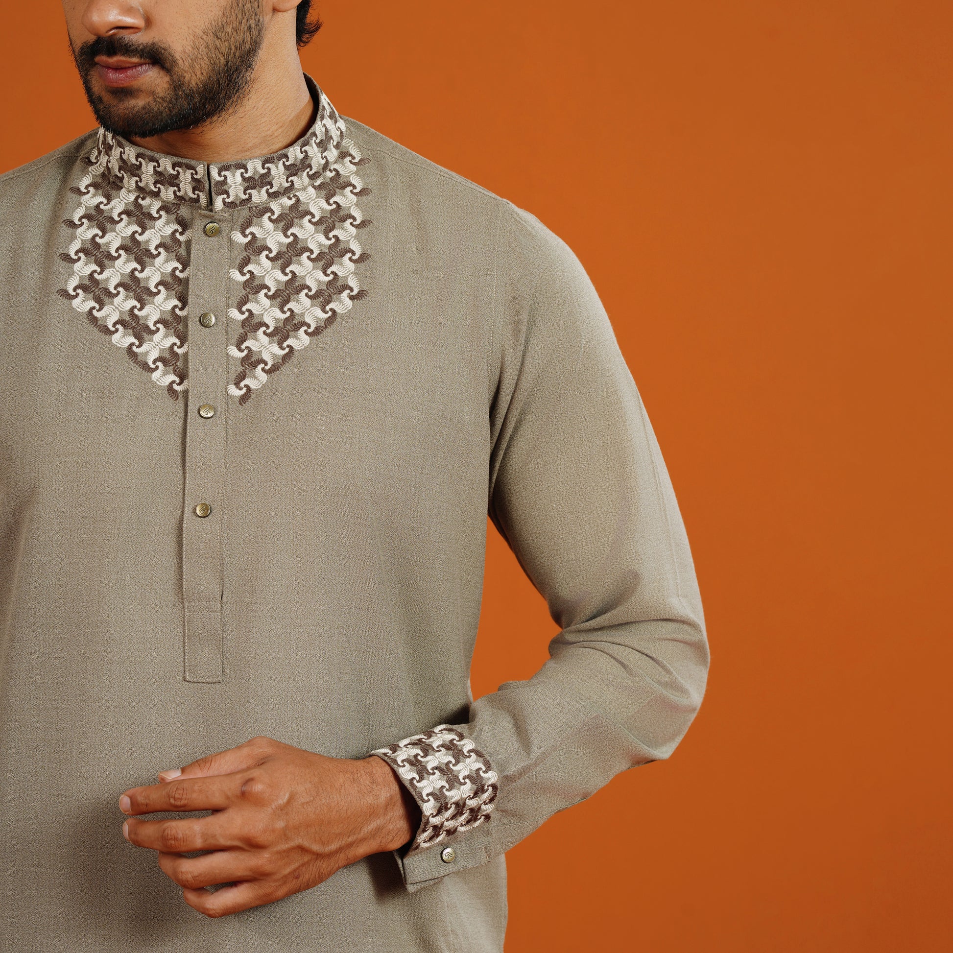 Man wearing a traditional outfit with intricate collar and sleeve designs on an orange background