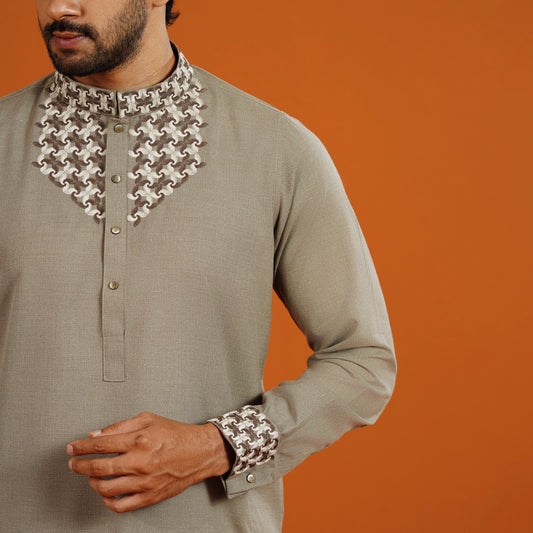 Man wearing a traditional outfit with intricate collar and sleeve designs on an orange background
