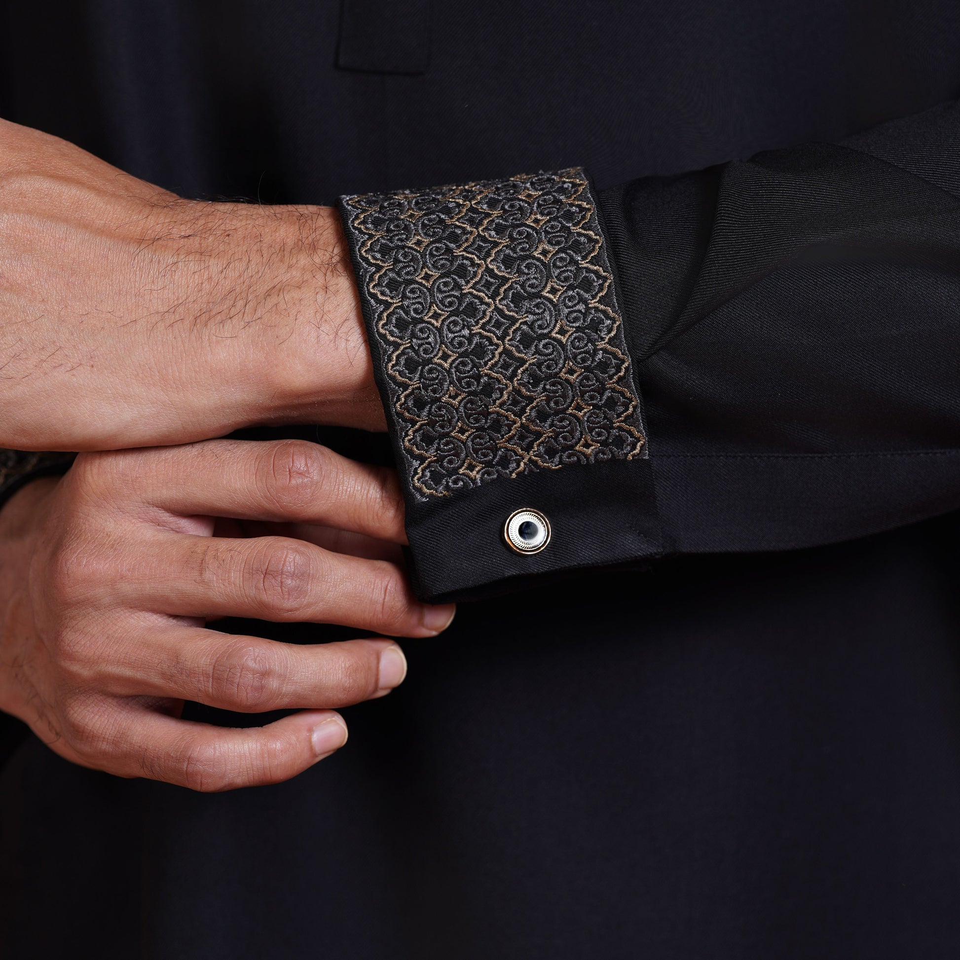 Close-up of a black shirt with an ornate cuff being adjusted by a hand.