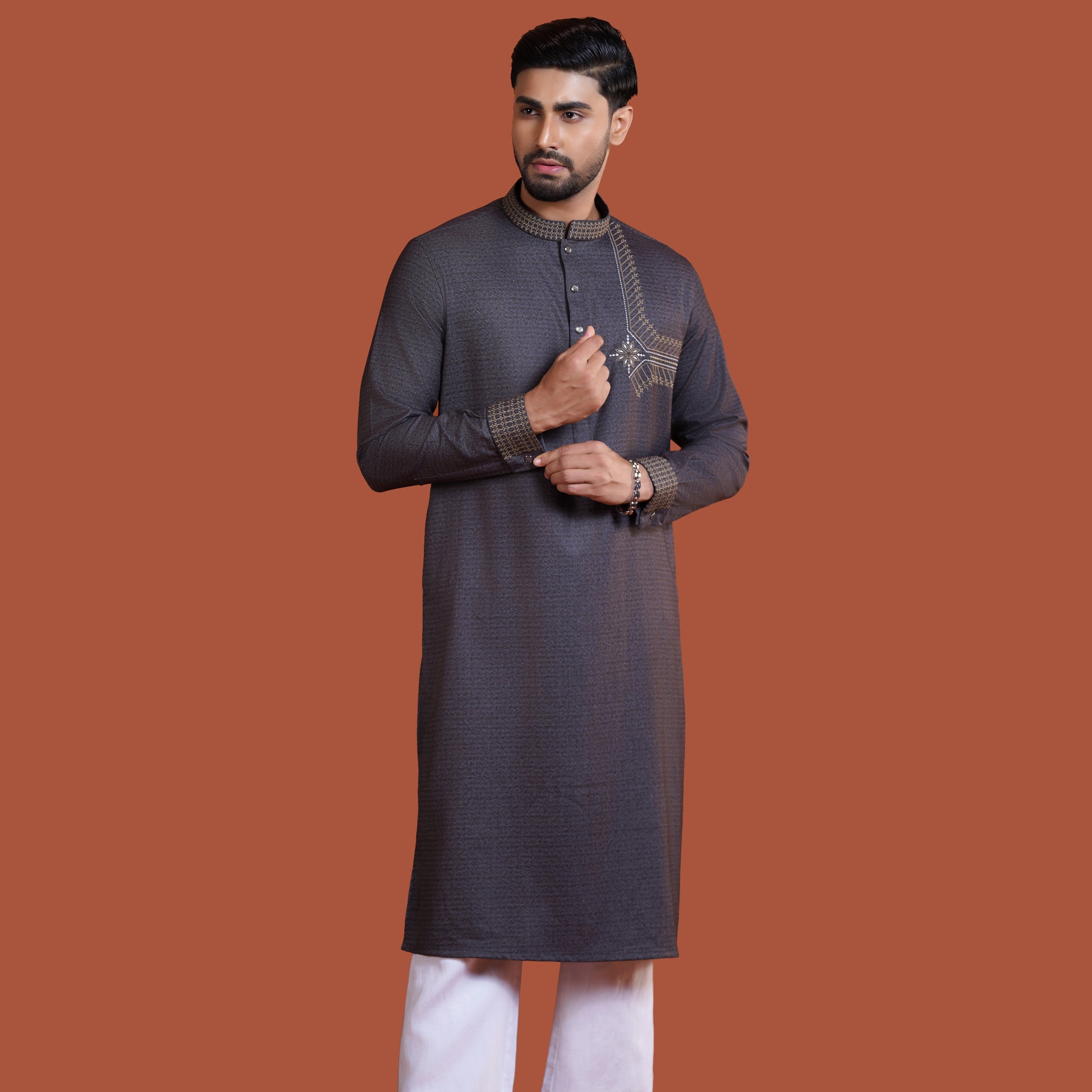 Man wearing a dark gray kurta with white pants on a brown background