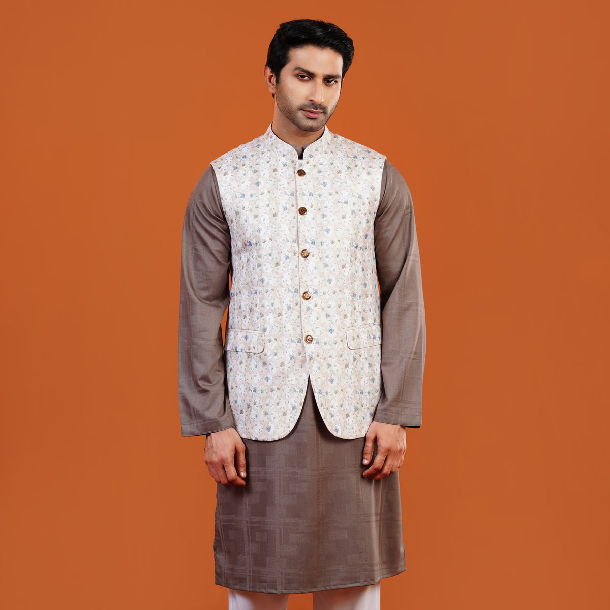 Man wearing a traditional outfit with a patterned vest on an orange background