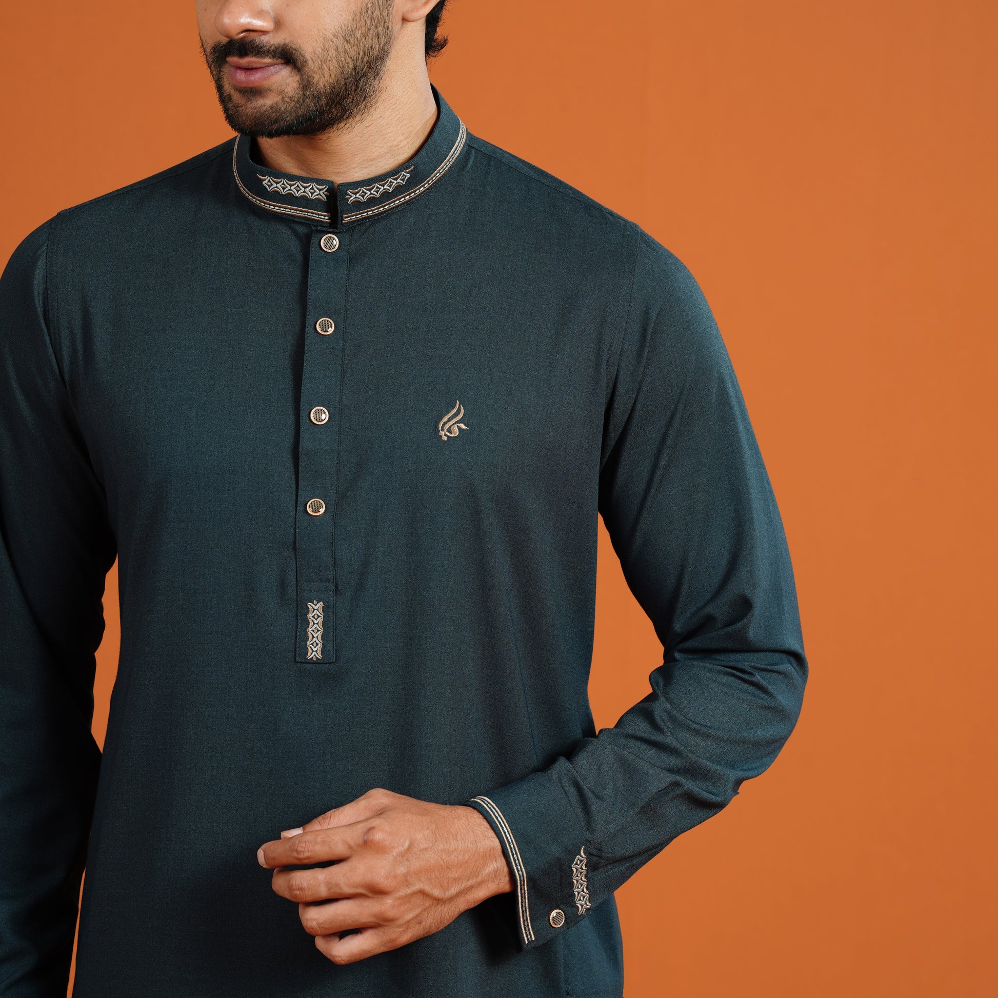 Man wearing a dark green long-sleeve shirt with decorative elements on an orange background