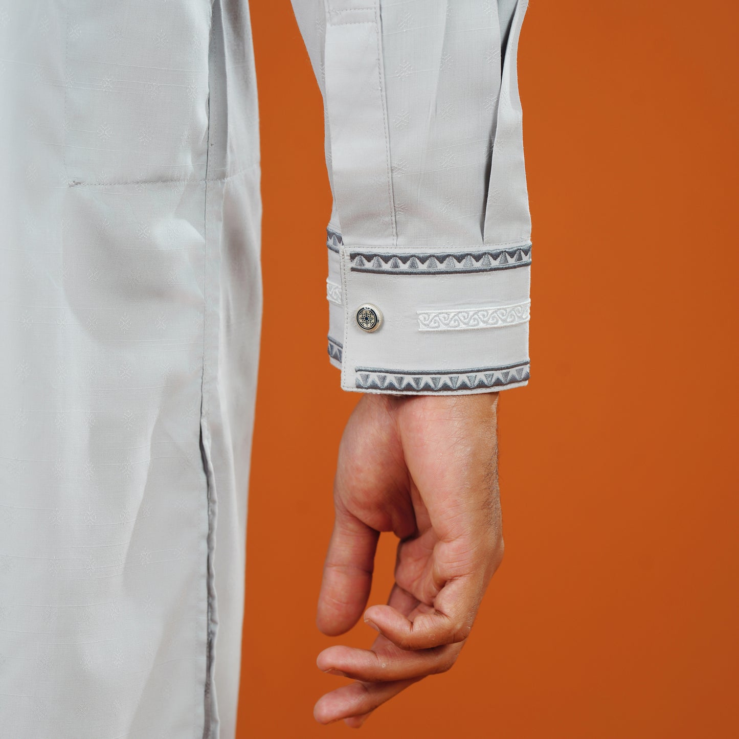 YAMAAN Close-up of a person wearing a light gray panjabi with a button on an orange background