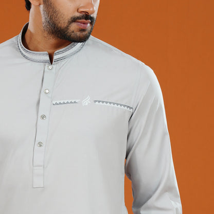 Man wearing a light gray traditional outfit with intricate details on an orange background