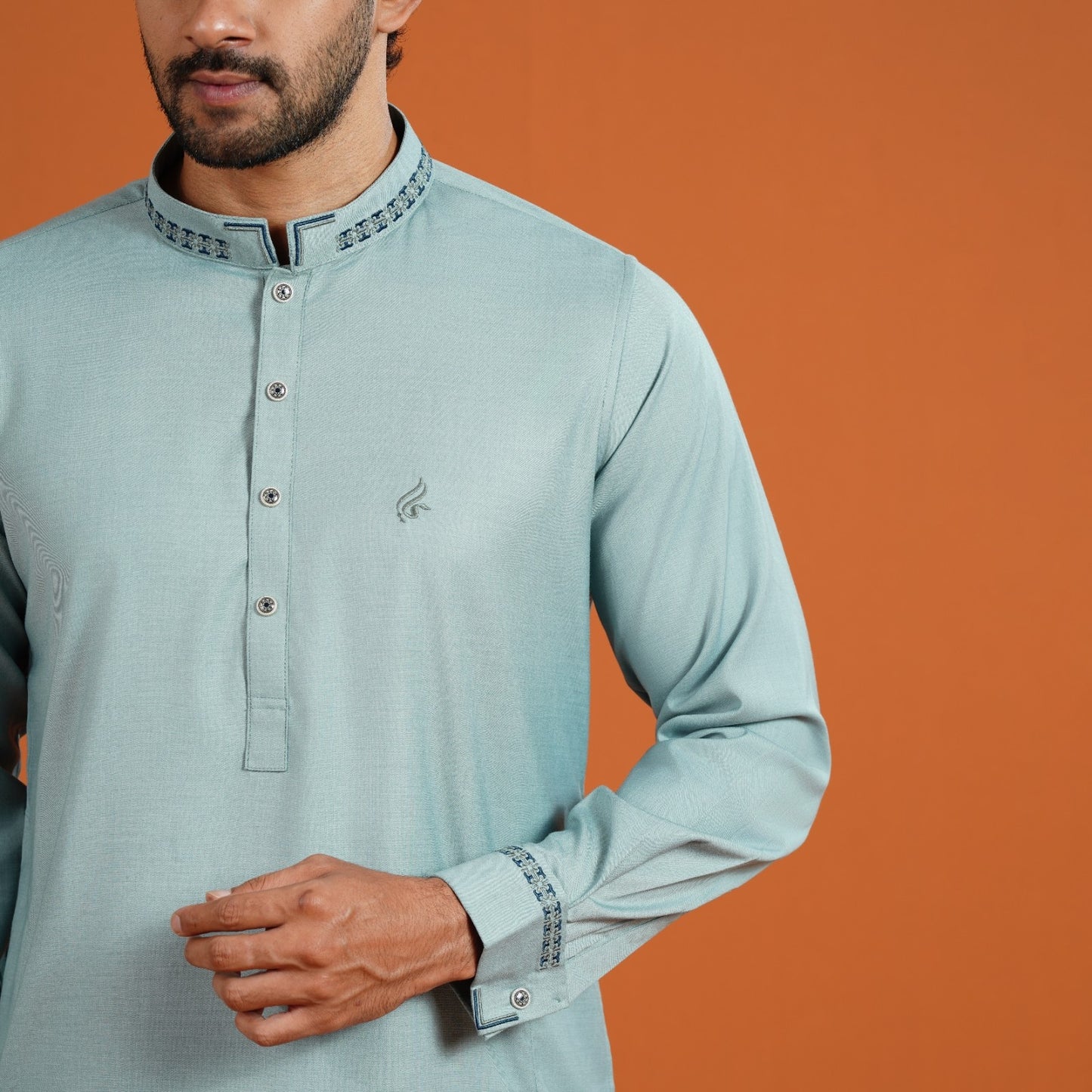 Man wearing a light blue kurta with intricate details on an orange background