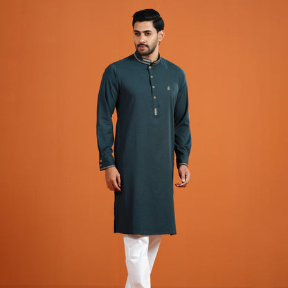 Man wearing a dark green kurta with white pants on an orange background
