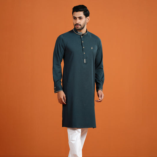 Man wearing a dark green kurta with white pants on an orange background