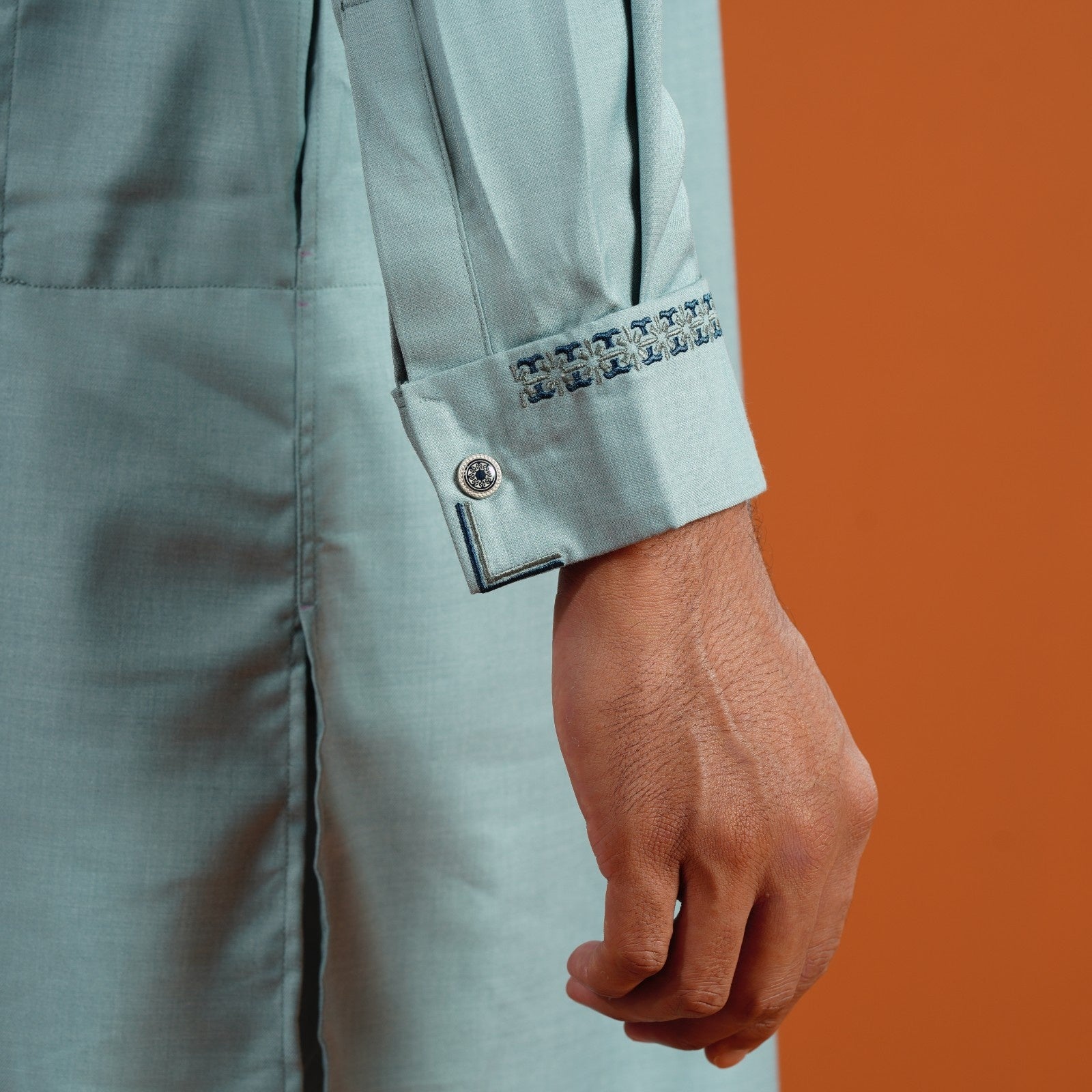 YAMAAN Light blue jacket with a hand wearing a watch on an orange background